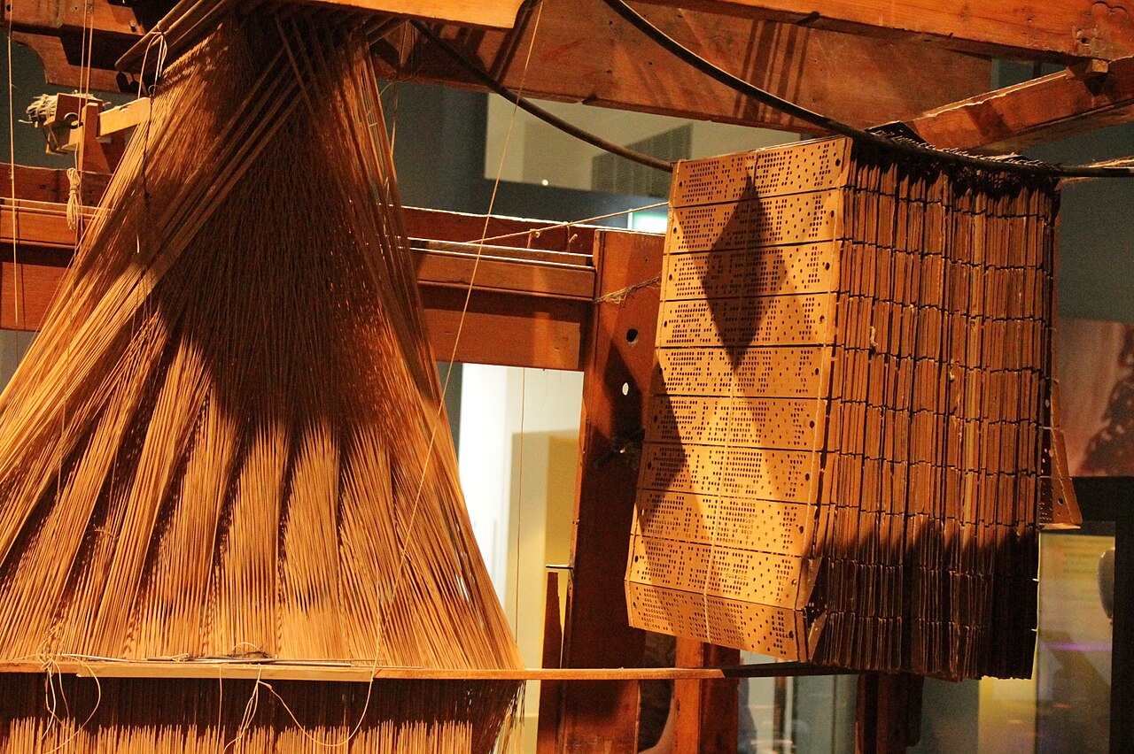 Jacquard loom with its punched cards — human intent encoded for a machine to execute